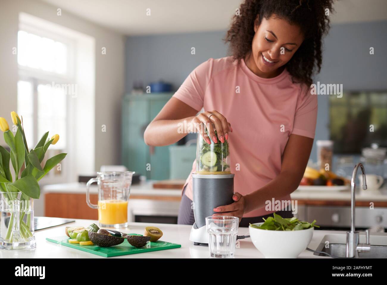 Woman Making Healthy Juice Drink With Fresh Ingredients In Electric Juicer After Exercise Stock Photo