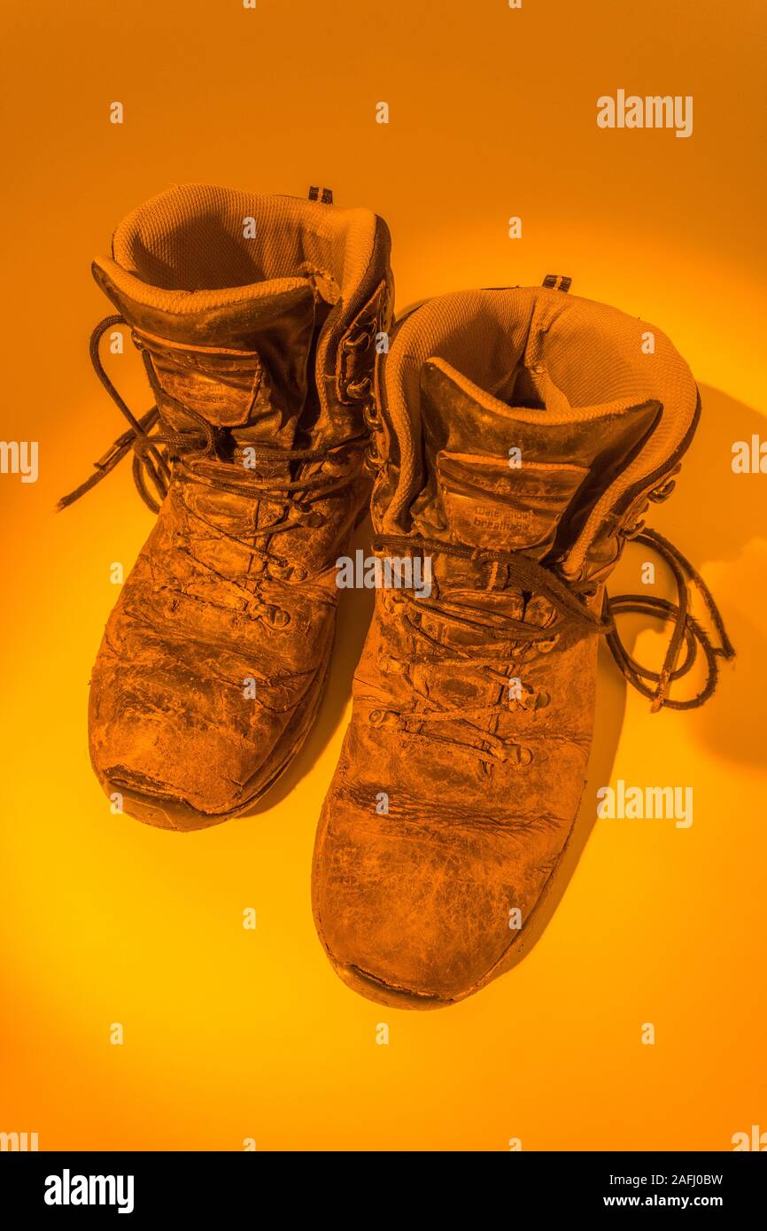 Pair of muddy walking boots bathed in orange pool of light. Metaphor hot footed perhaps, or tired feet, pounding the beat, abstract footwear. Stock Photo