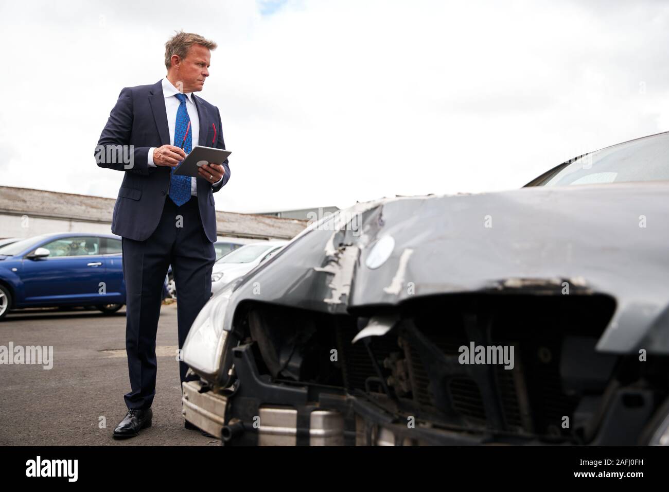 Male Insurance Loss Adjuster With Digital Tablet Inspecting Damage To Car From Motor Accident Stock Photo