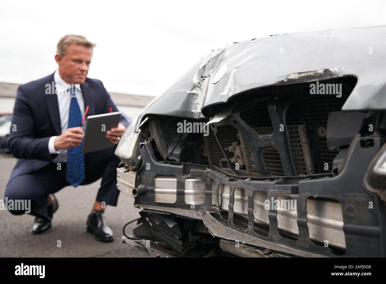 Male Insurance Loss Adjuster With Digital Tablet Inspecting Damage To Car From Motor Accident Stock Photo