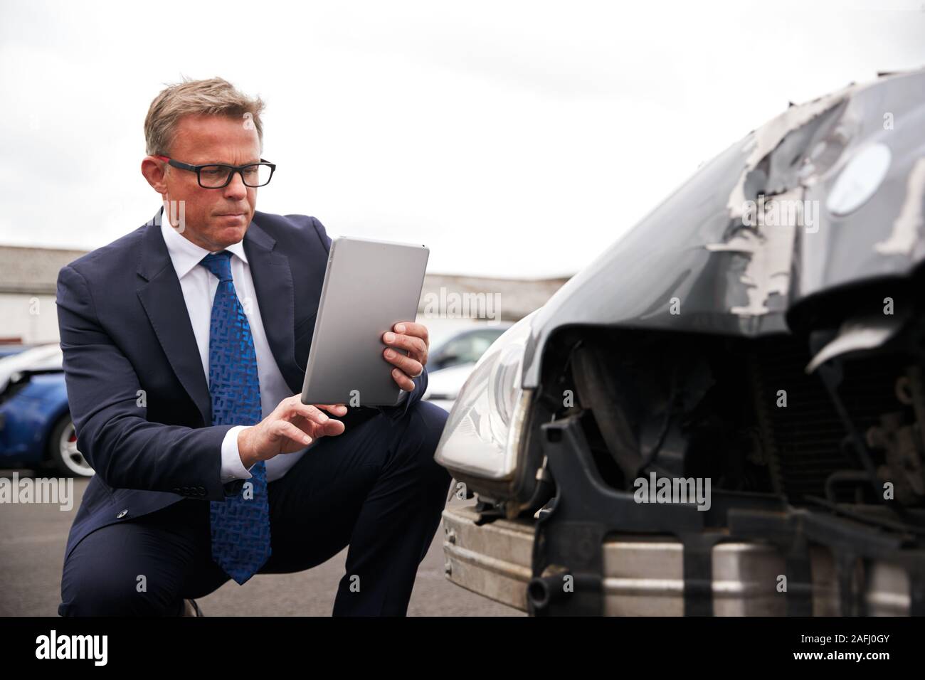 Insurance Loss Adjuster Taking Picture With Digital Tablet Of Damage To Car From Motor Accident Stock Photo
