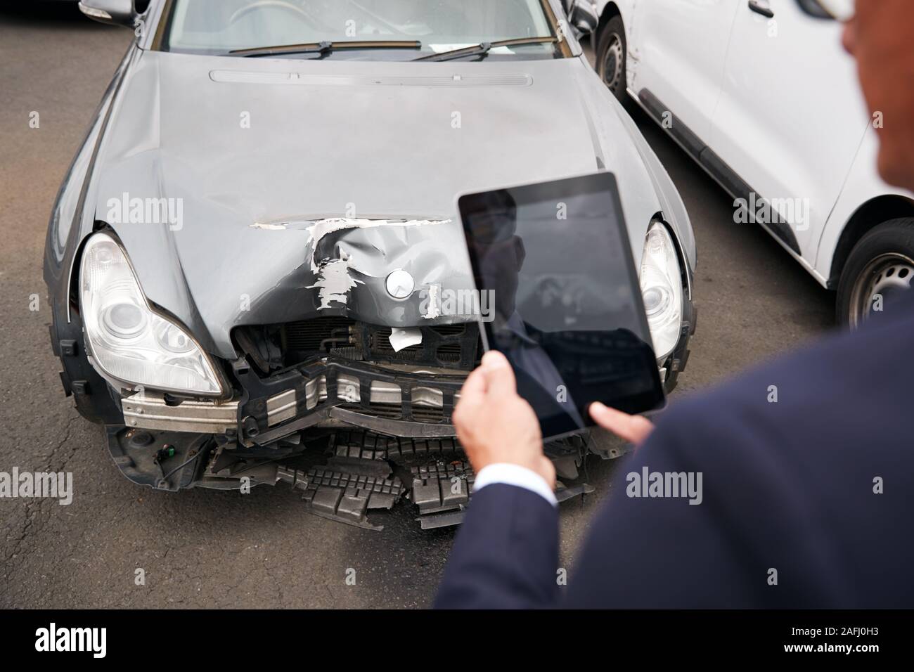 Insurance Loss Adjuster Taking Picture With Digital Tablet Of Damage To Car From Motor Accident Stock Photo