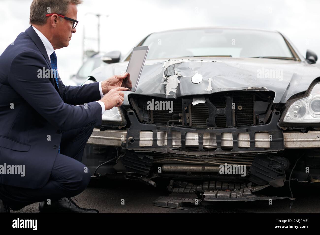 Male Insurance Loss Adjuster With Digital Tablet Inspecting Damage To Car From Motor Accident Stock Photo