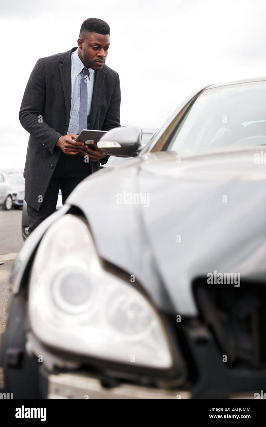 Male Insurance Loss Adjuster With Digital Tablet Inspecting Damage To Car From Motor Accident Stock Photo