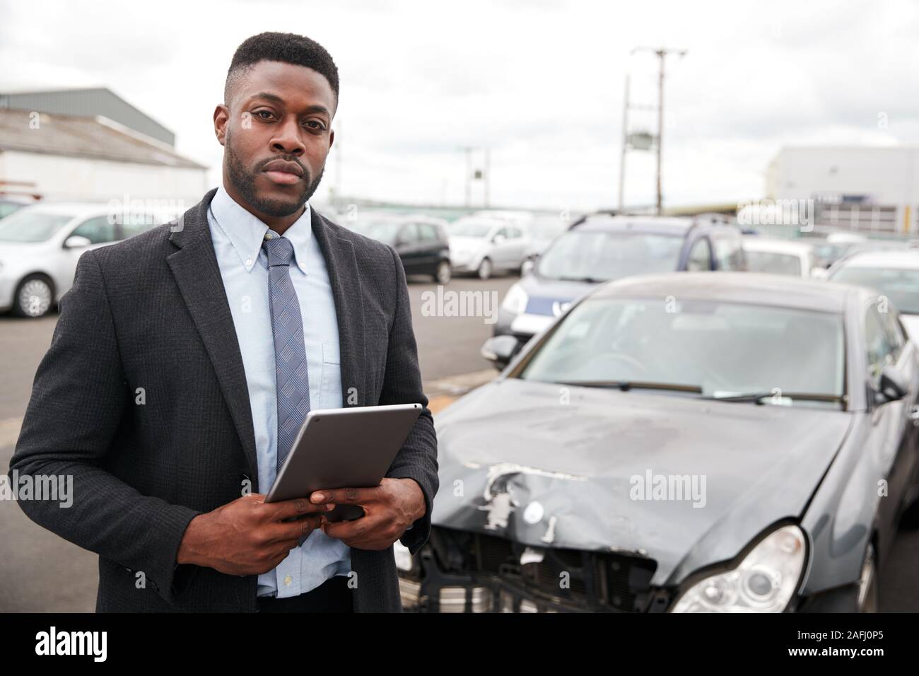 Portrait Of Insurance Loss Adjuster With Digital Tablet Inspecting Damage To Car From Motor Accident Stock Photo