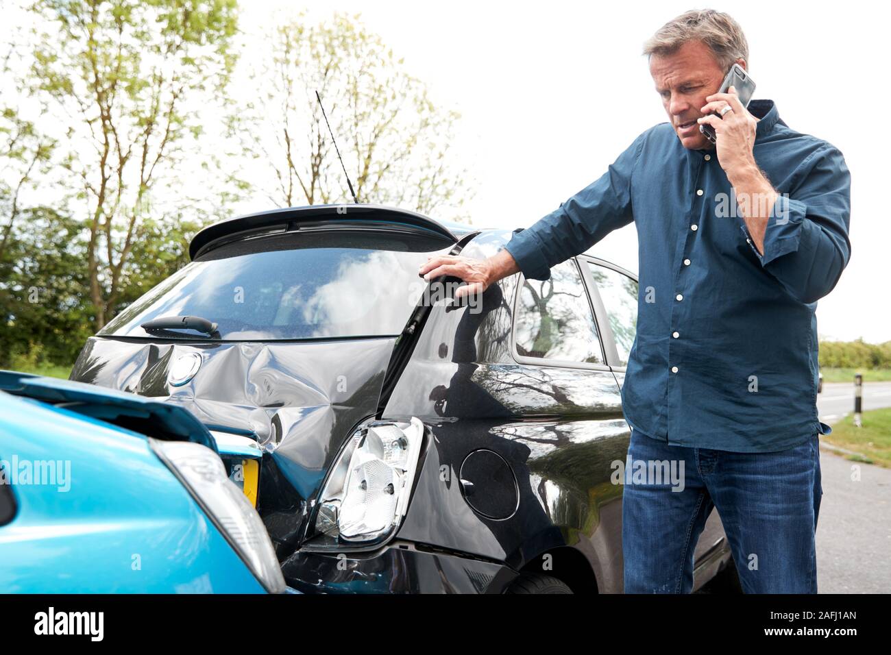Mature Male Motorist Involved In Car Accident Calling Insurance Company Or Recovery Service Stock Photo