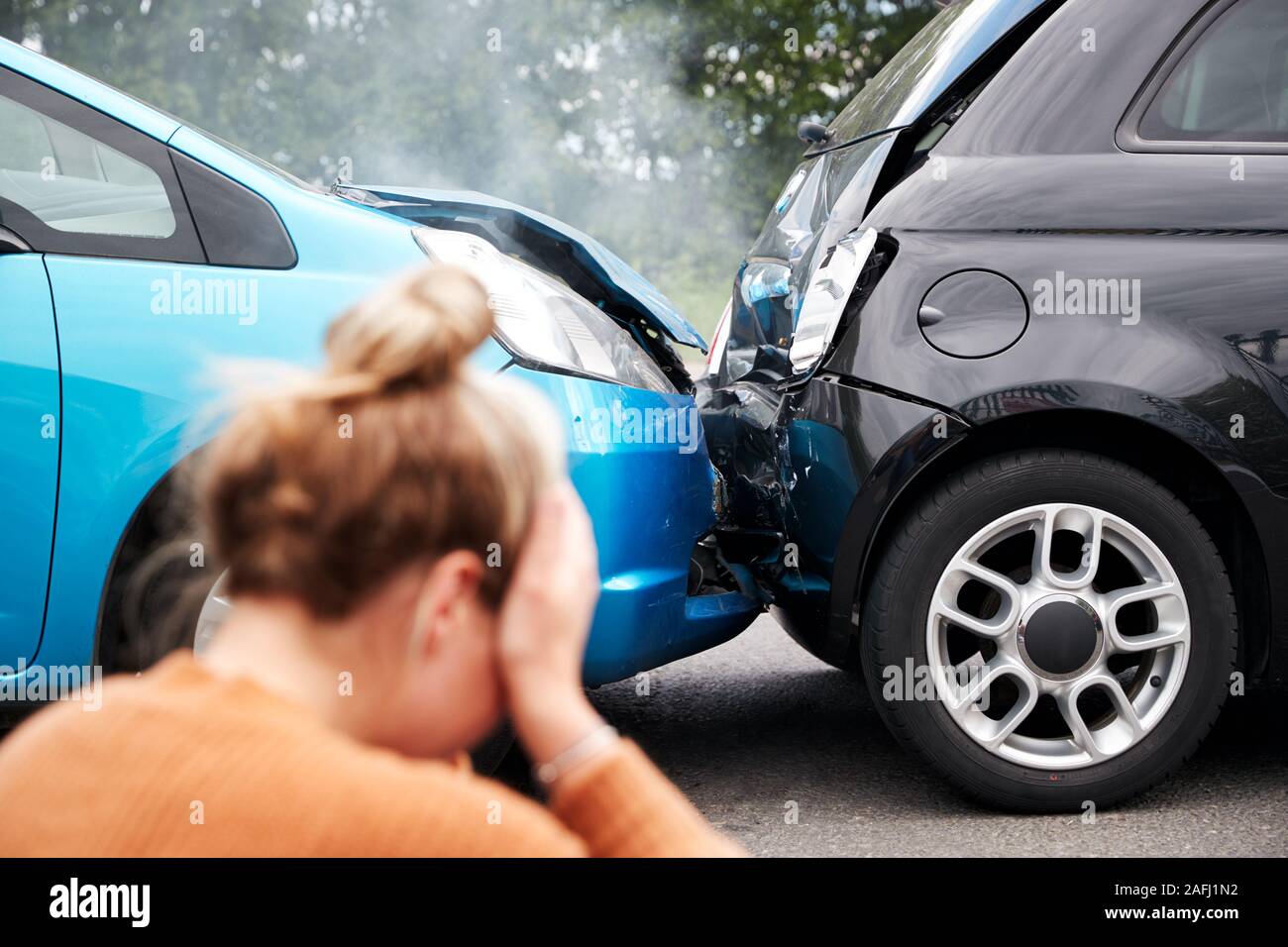 Female Motorist With Head In Hands Sitting Next To Vehicles Involved In Car Accident Stock Photo