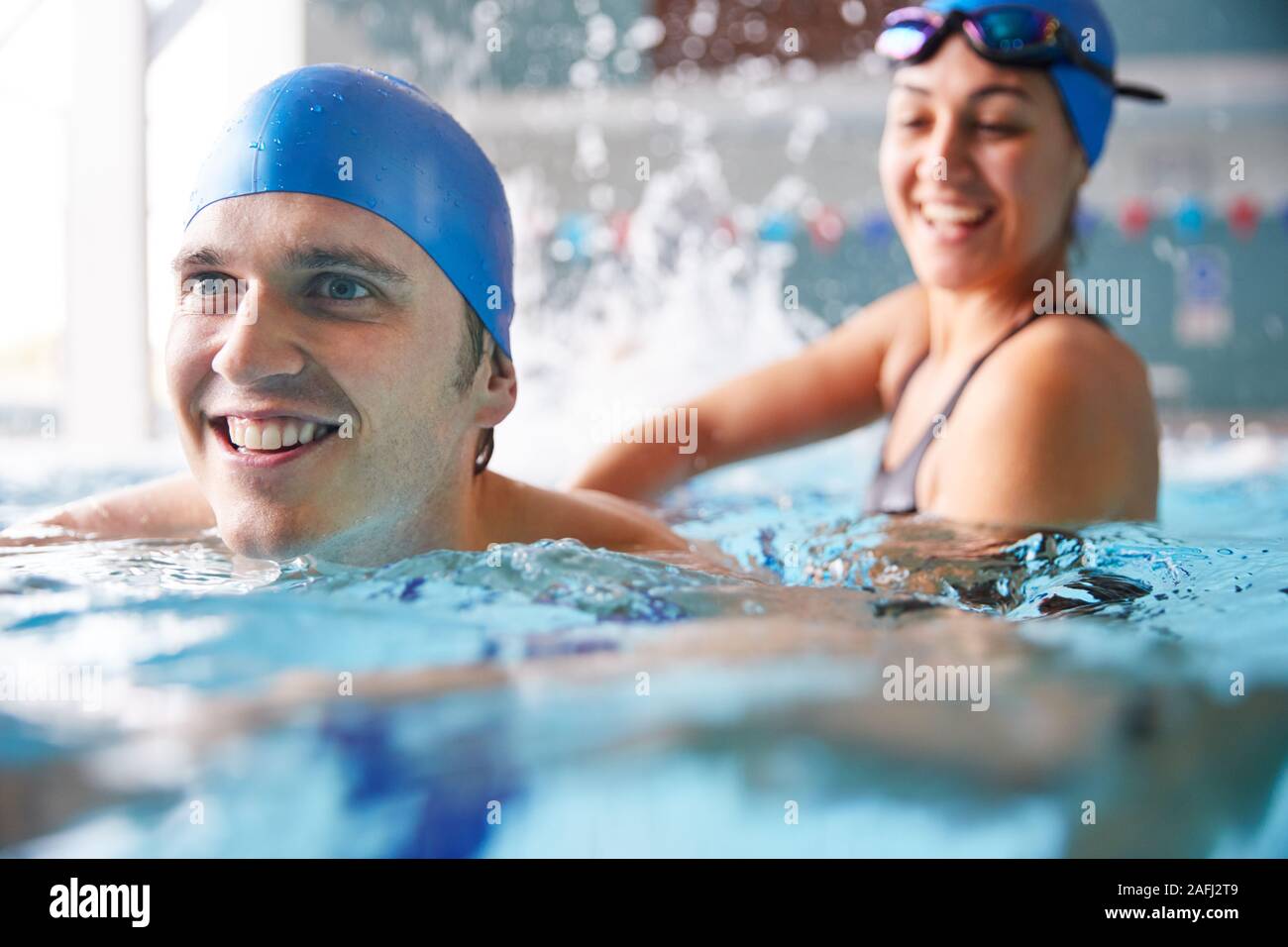 Female Swimming Teacher Giving Man One To One Lesson In Pool Stock Photo