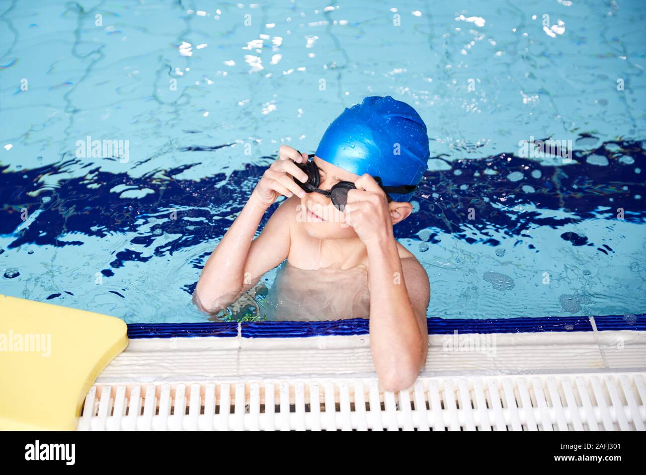 Boy With Float Resting On Edge Of Swimming Pool During Lesson Stock Photo