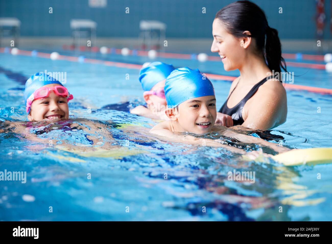 Female Coach In Water Giving Group Of Children Swimming Lesson In Indoor Pool Stock Photo