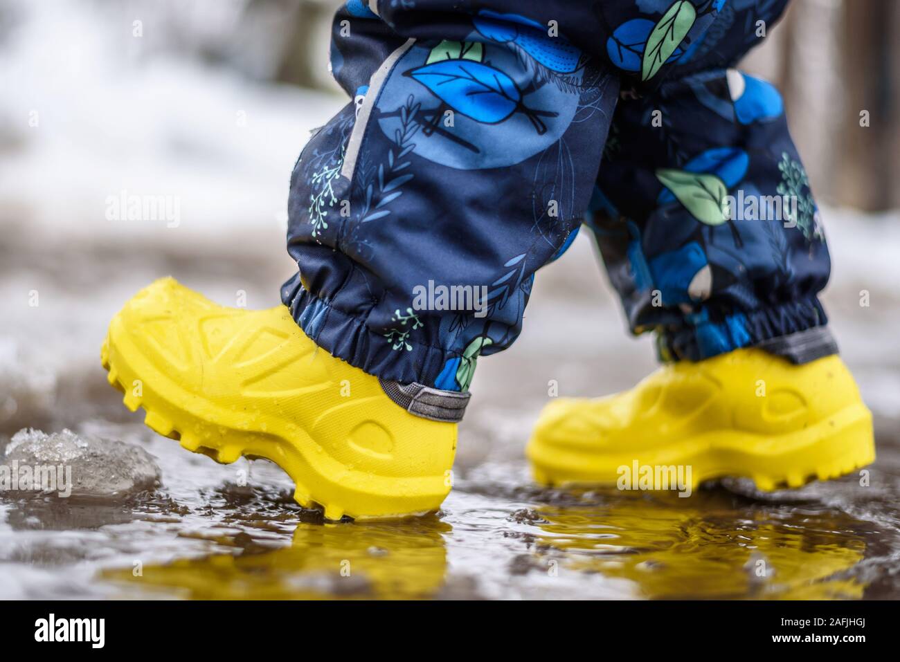 little boy in yellow rubber walks through puddles in spring Stock Photo ...