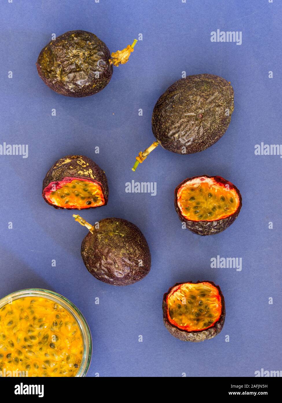 Lay flat composition showing a whole and sliced passion fruit and passion fruit pulp on a blue background Stock Photo