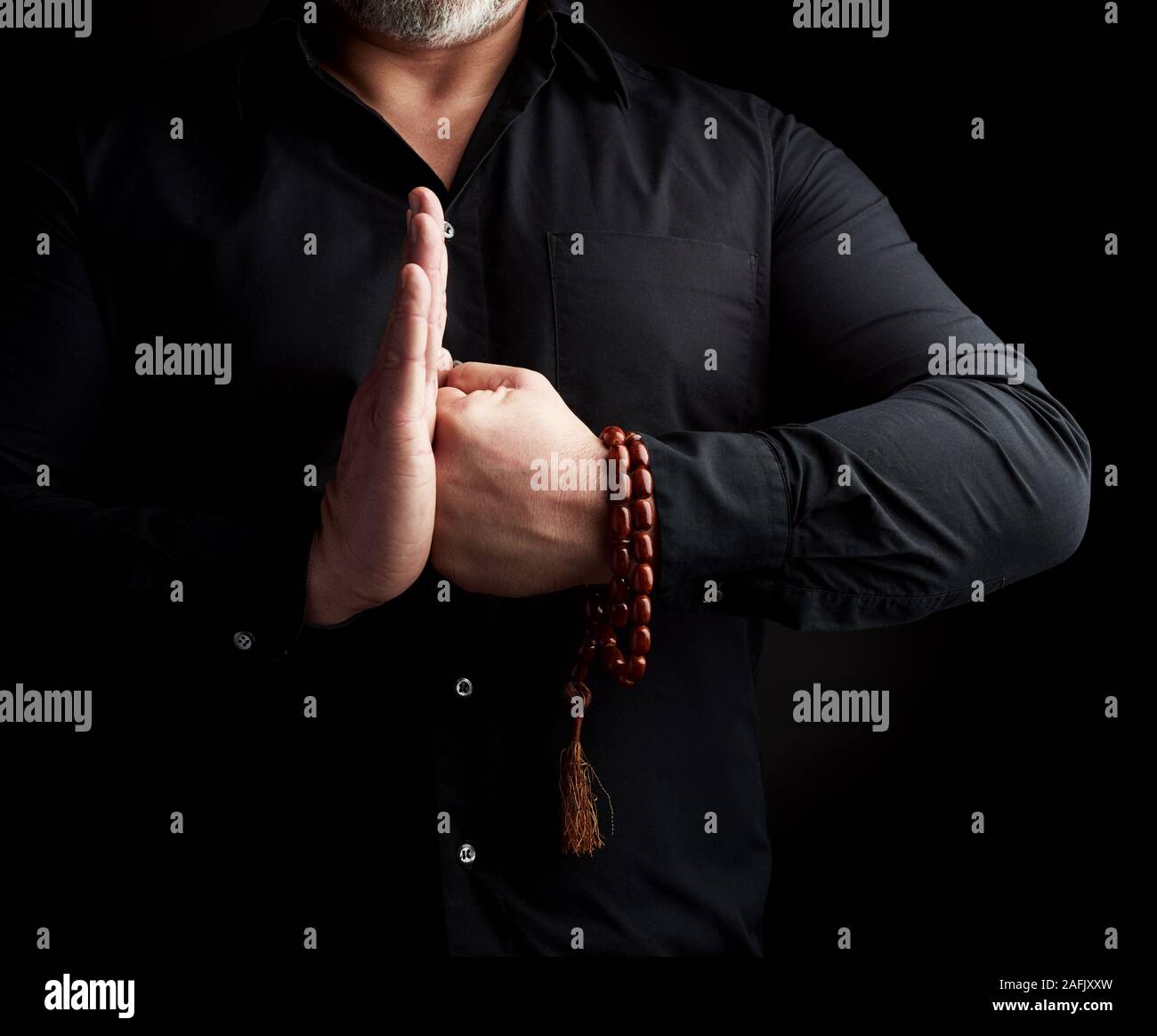 adult man in black clothes joined hands in front of chest, dark background Stock Photo