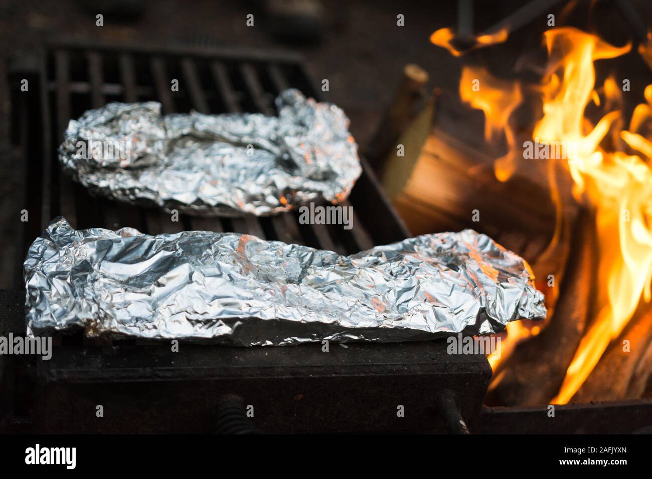 Delicious meal wrapped in tin foil cooking over fire at campsite Stock