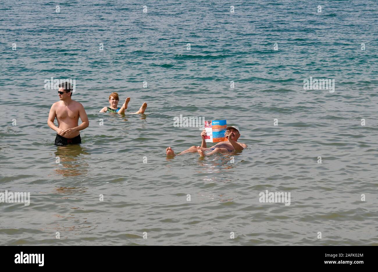Dead Sea, Jordan - March 05, 2019: Unidentified people enjoy swim and reading newspaper in Dead Sea, a salt lake 400m below sea level, water and mud i Stock Photo