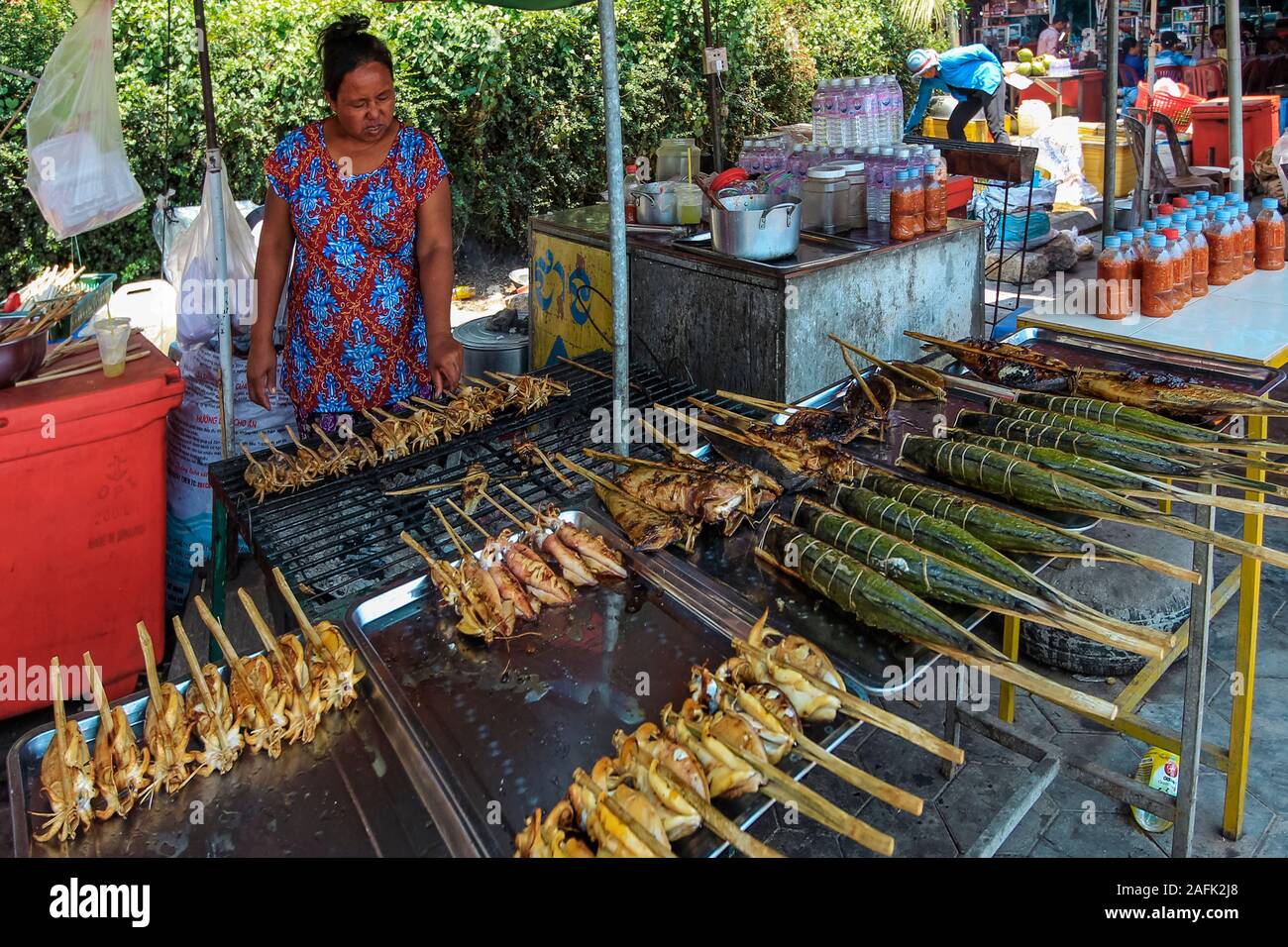 Woman with stall of barbecued fish & squid on sticks at the Crab Market in this resort town, famous for it's seafood; Kep, Cambodia Stock Photo