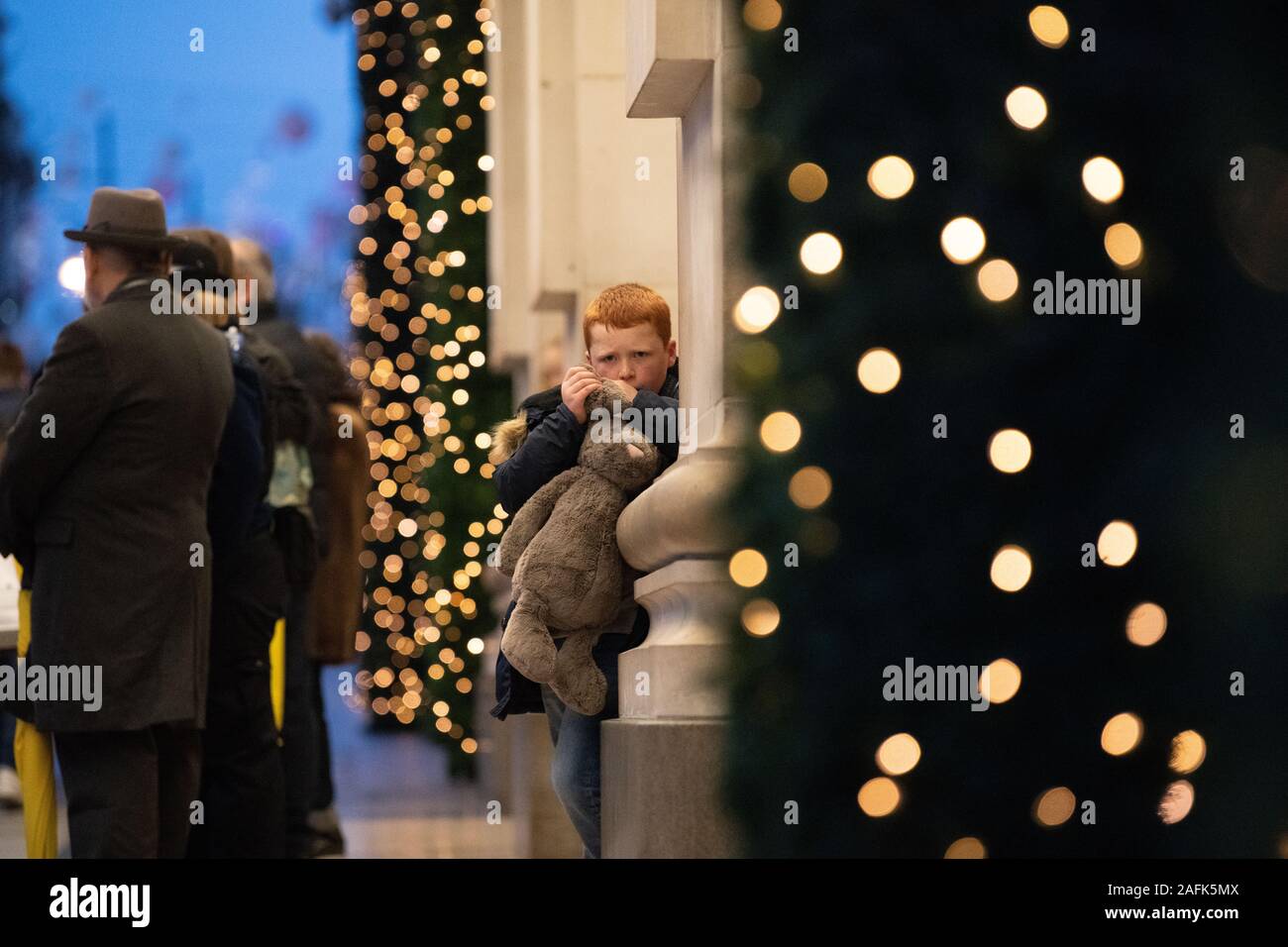 Small ginger hair boy holding a large soft toy bunny outside Selfridges looking at camera. Christmas lights and decorations in the background. London Stock Photo