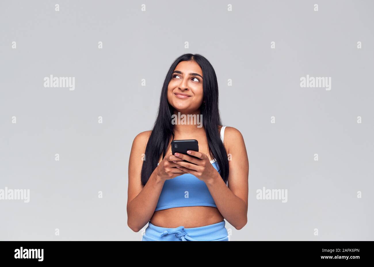 Studio Shot Of Causally Dressed Young Woman Using Mobile Phone Looking Off Camera Stock Photo