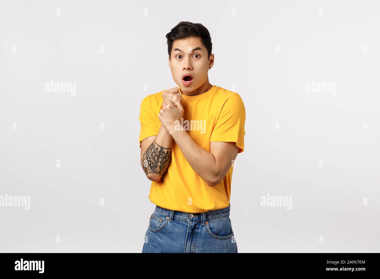 Sensetive and shocked, scared young asian guy with tattoos, pull hand back, press arm to chest insecure and afraid, gasping open mouth, look like Stock Photo