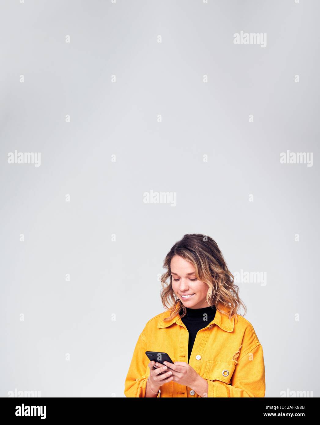 Studio Shot Of Smiling Causally Dressed Young Woman Using Mobile Phone Stock Photo