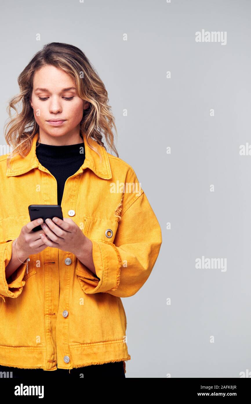 Studio Shot Of Causally Dressed Young Woman Using Mobile Phone Stock Photo