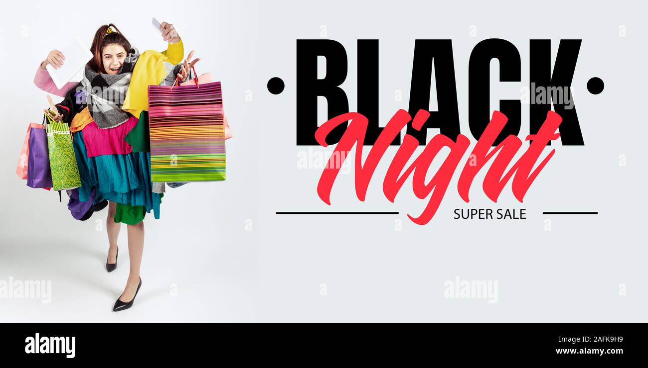 Black night finance concept. Woman addicted of sales and clothes. Female model wearing too much colorful clothes. Fashion style black friday sale purchases money online buying. Flyer for ad Stock Phot...