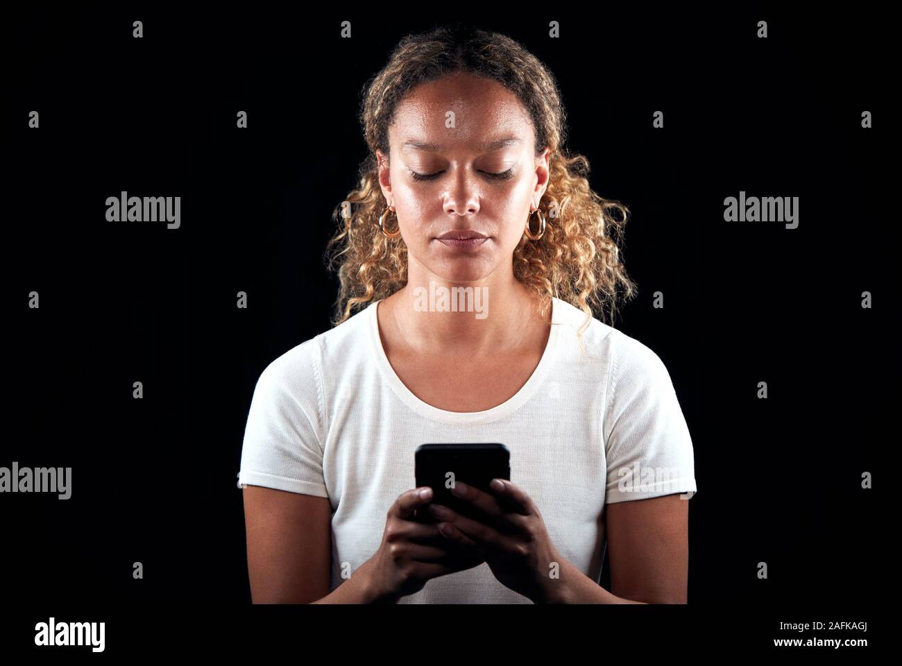 Studio Shot Of Unhappy Woman Holding Mobile Phone Being Bullied Online Stock Photo