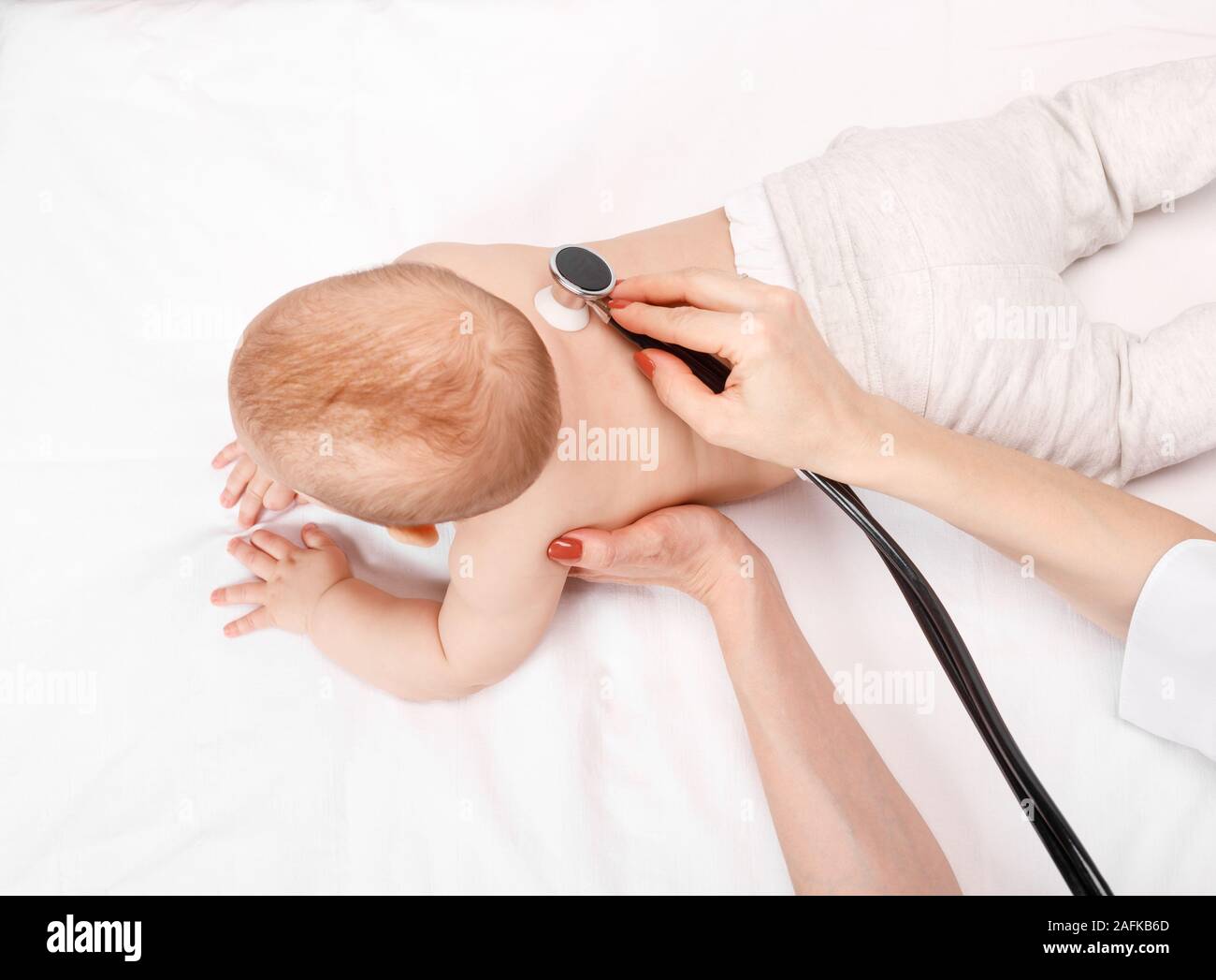 Pediatrician examines happy six month baby's chest in pediatric clinic. Doctor using a