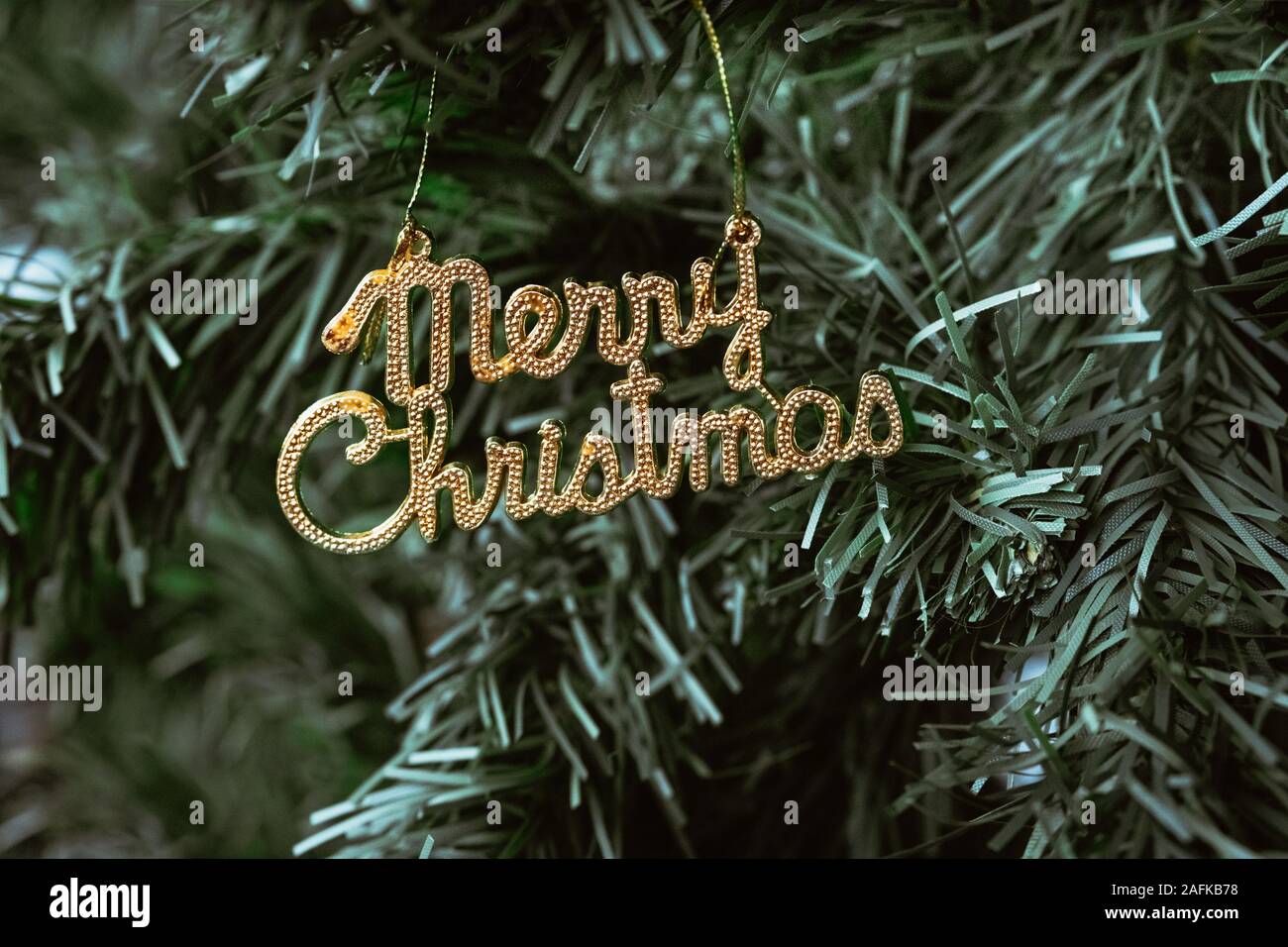 Close up of a golden English text "Merry Christmas" ornament hanging on Christmas tree. Stock Photo