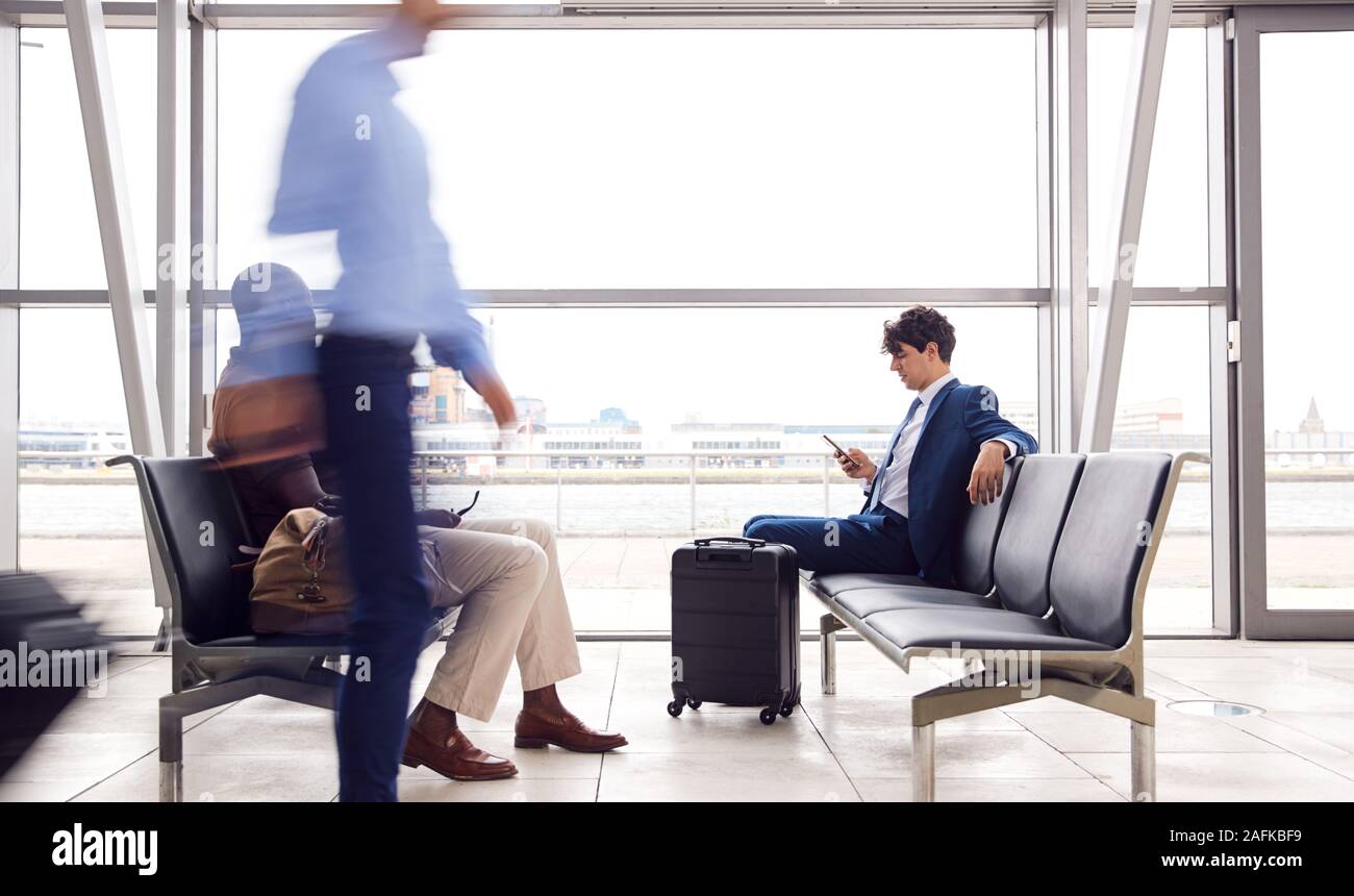 Businessman Sitting In Busy Airport Departure Lounge Using Mobile Phone Stock Photo