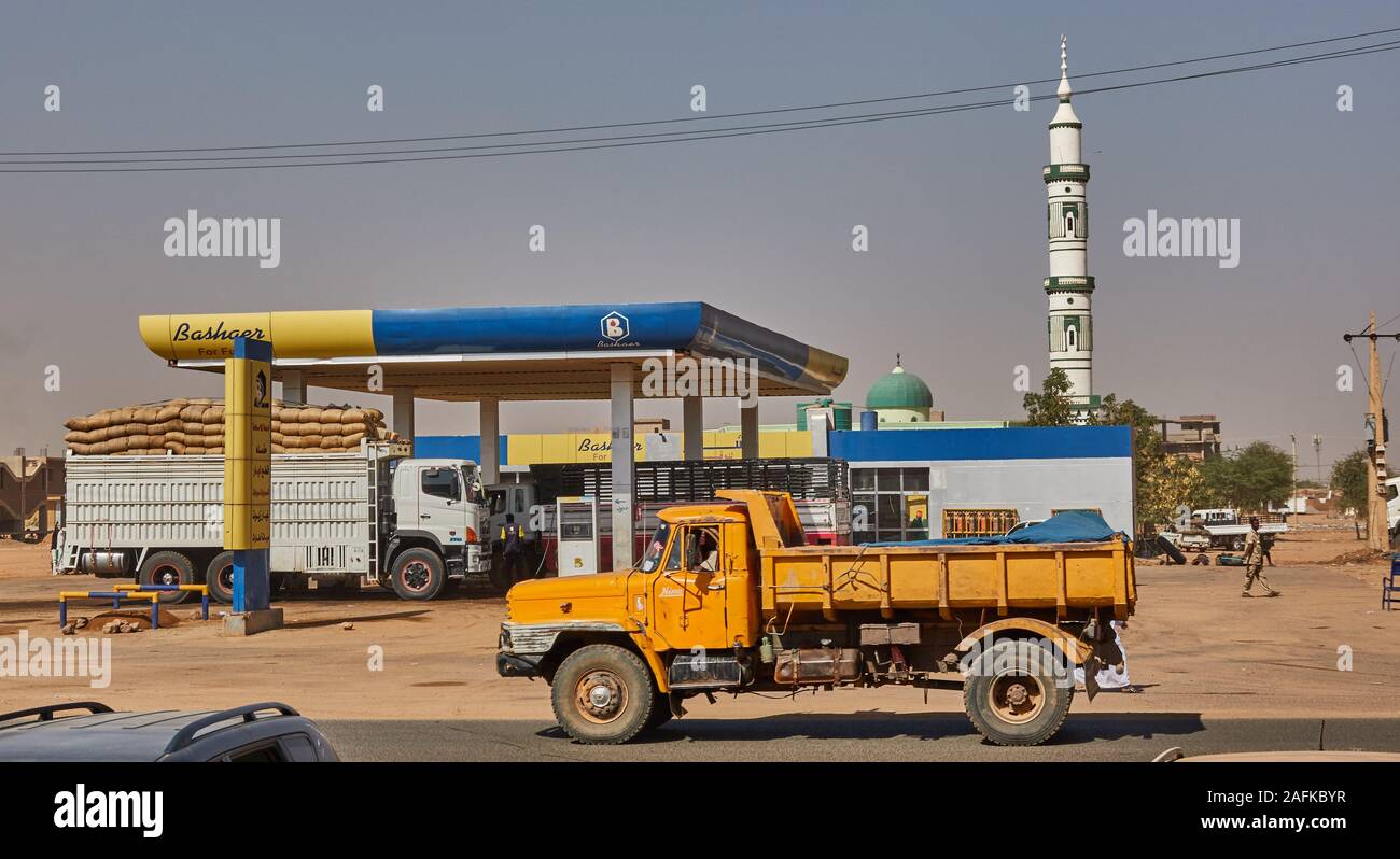 Khartoum, Sudan, ca. February 8., 2019: Yellow truck at a filling station in a desert village in front of a mosque with white minaret Stock Photo