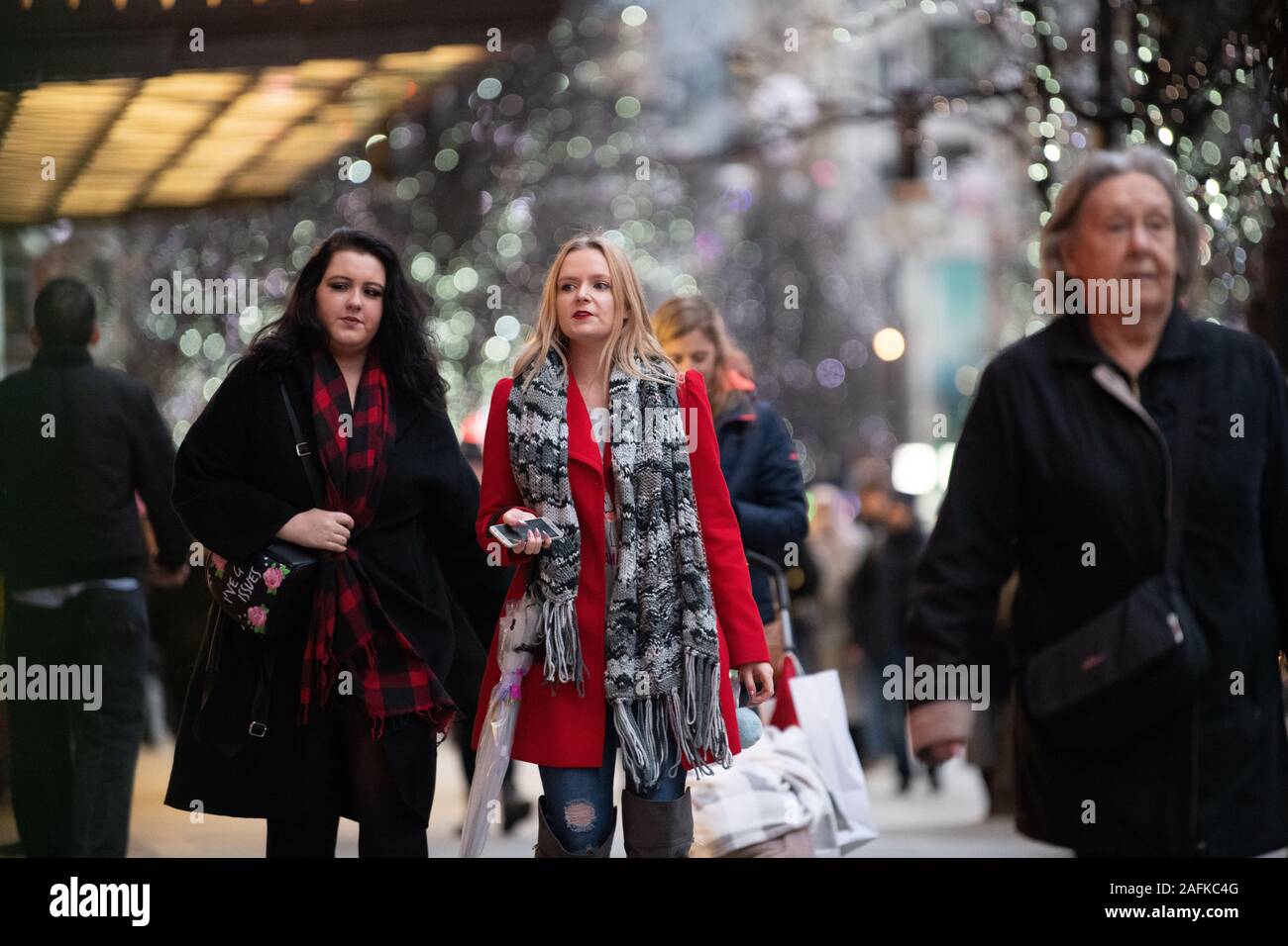 Christmas shoppers, one wearing a red coat, doing late Christmas shopping, outside Selfridges, Oxford Street, London, UK Stock Photo
