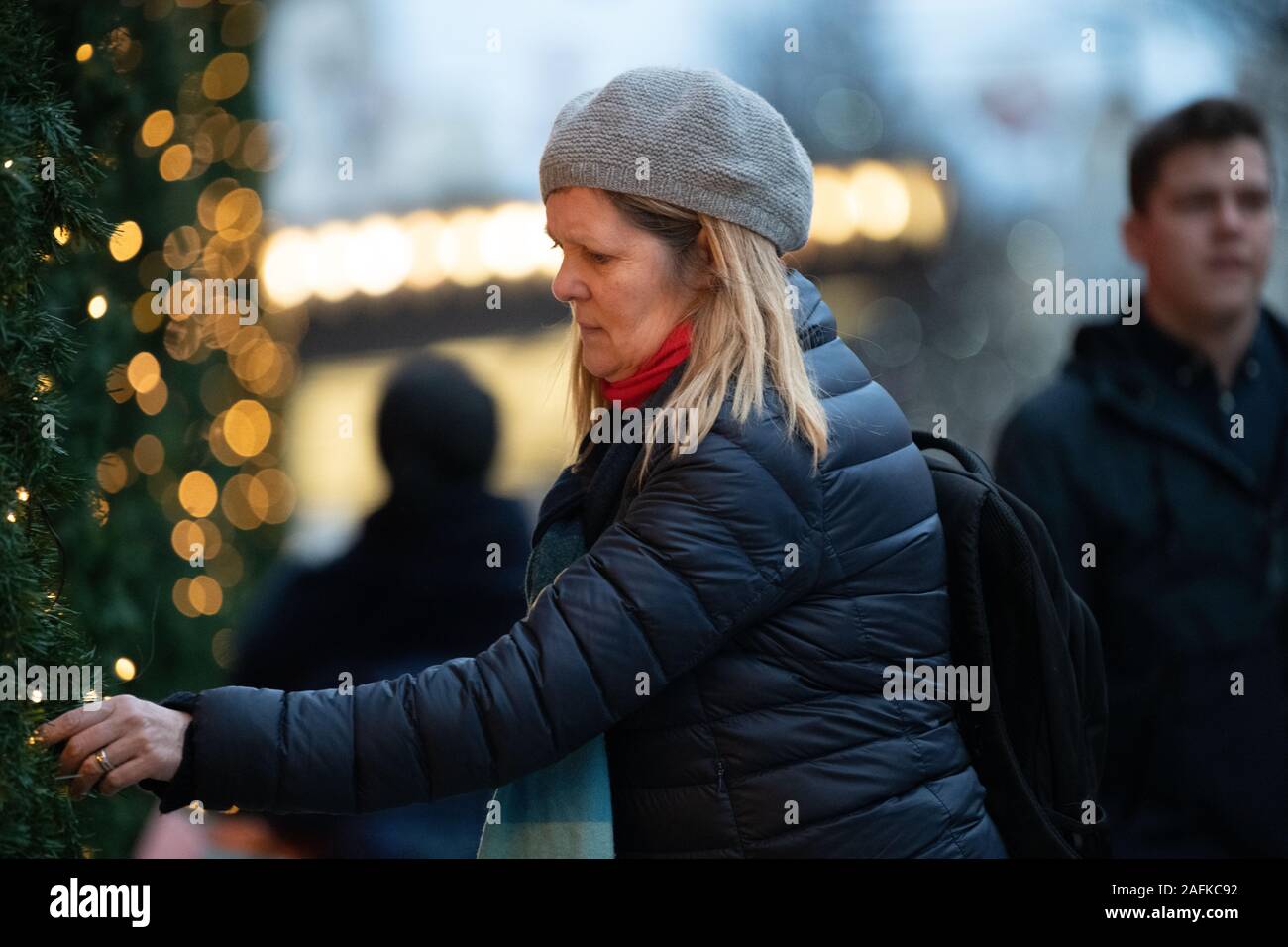 Woman in a hat touching the Christmas tree branches outside Selfridges, iconic Selfridges entrance in the background and passers by, London, UK Stock Photo