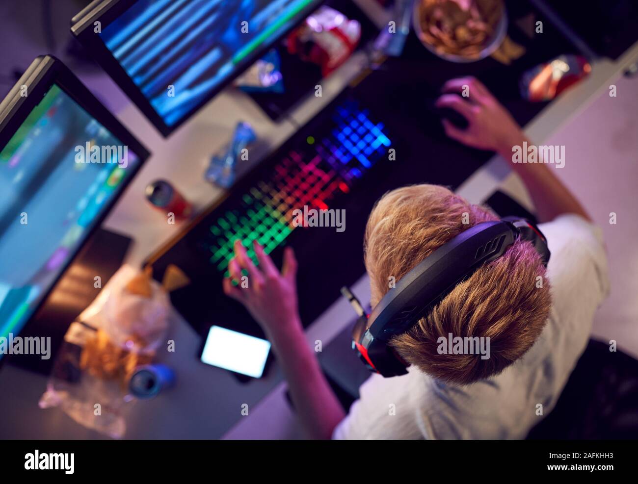 Overhead View Of Teenage Hacker Sitting In Front Of Computer Screens