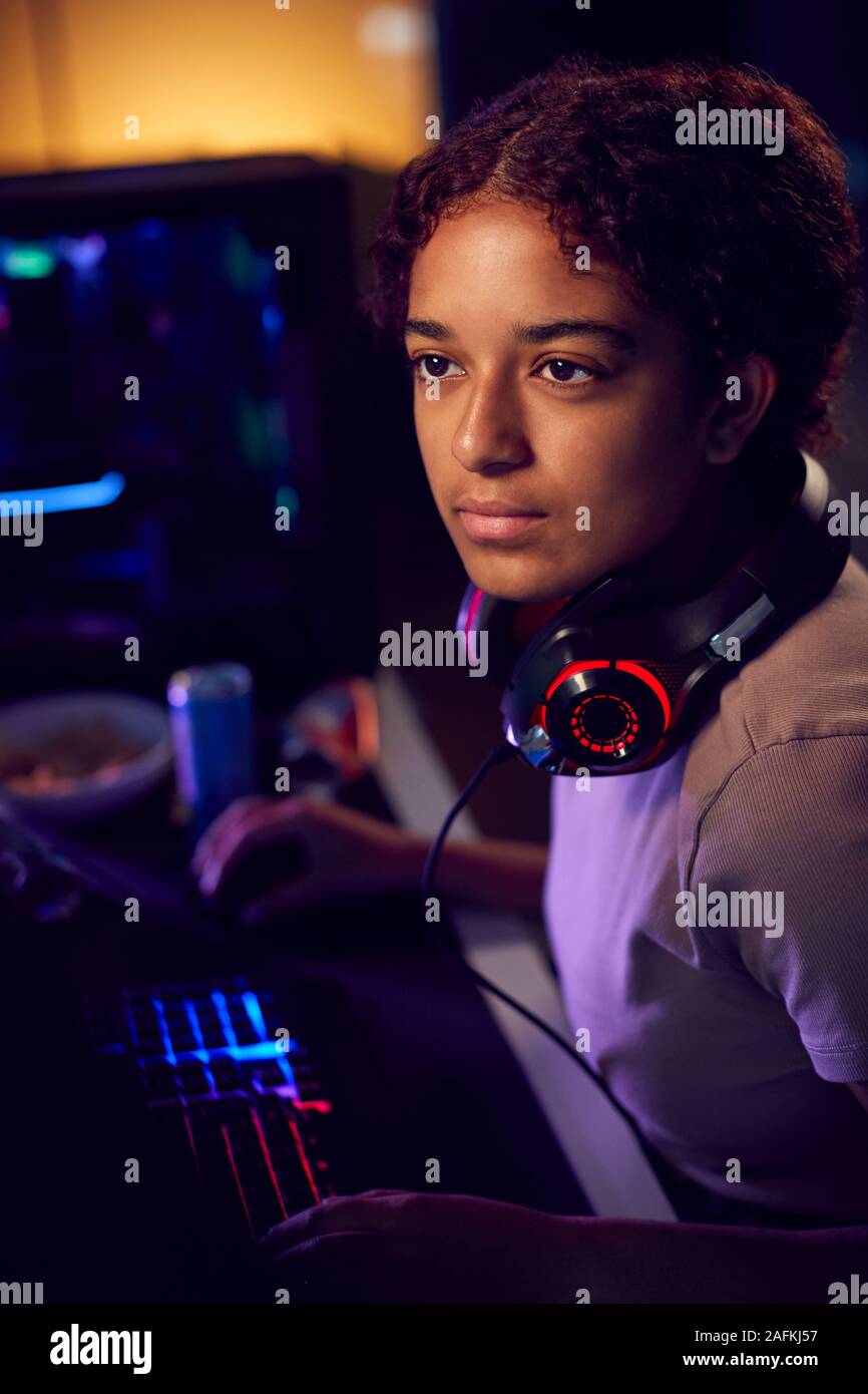 Teenage Girl With Headset Gaming At Home Using Dual Computer Screens