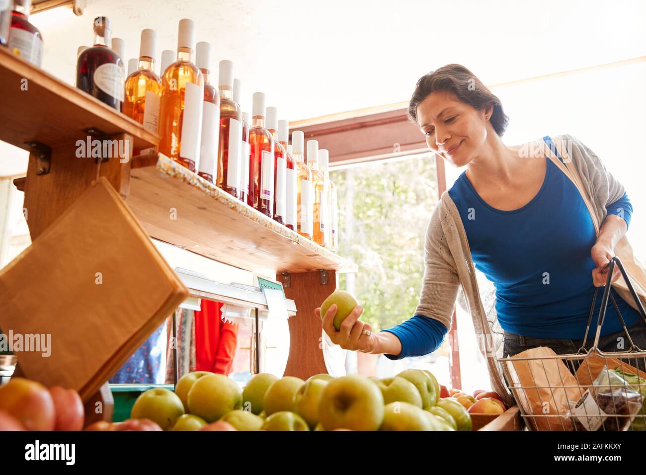 Female Customer With Shopping Basket Buying Fresh Apples In Organic Farm Shop Stock Photo