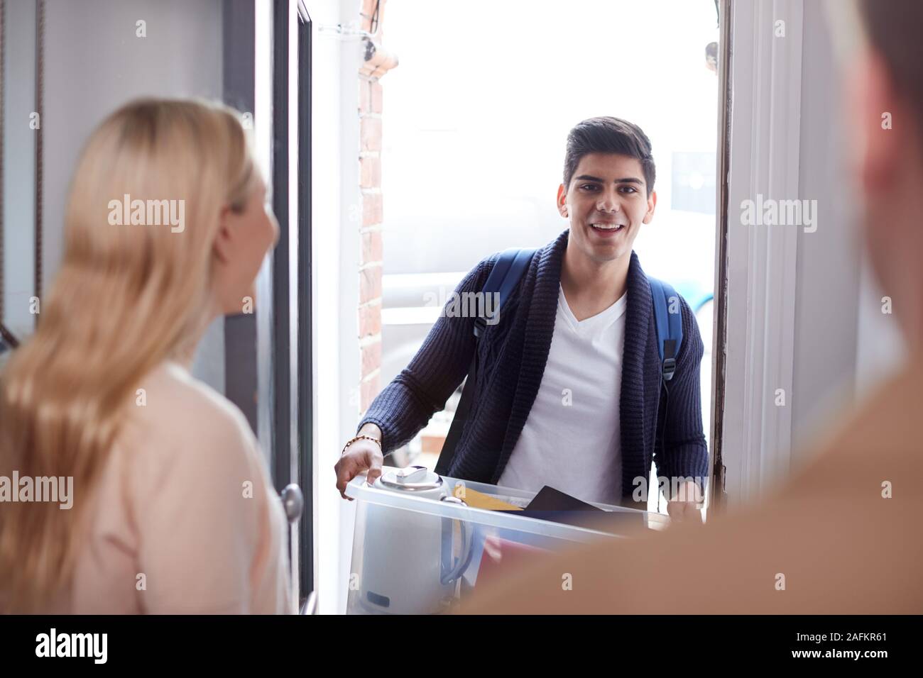 Male College Student Carrying Box Moving Into Accommodation Meeting House Mates Stock Photo