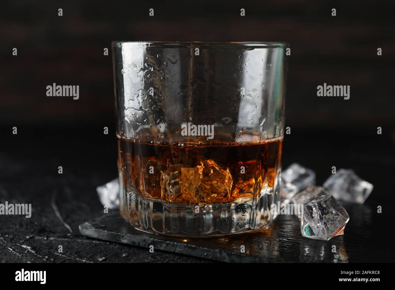 Glass of whiskey and ice cubes on black background, close up Stock