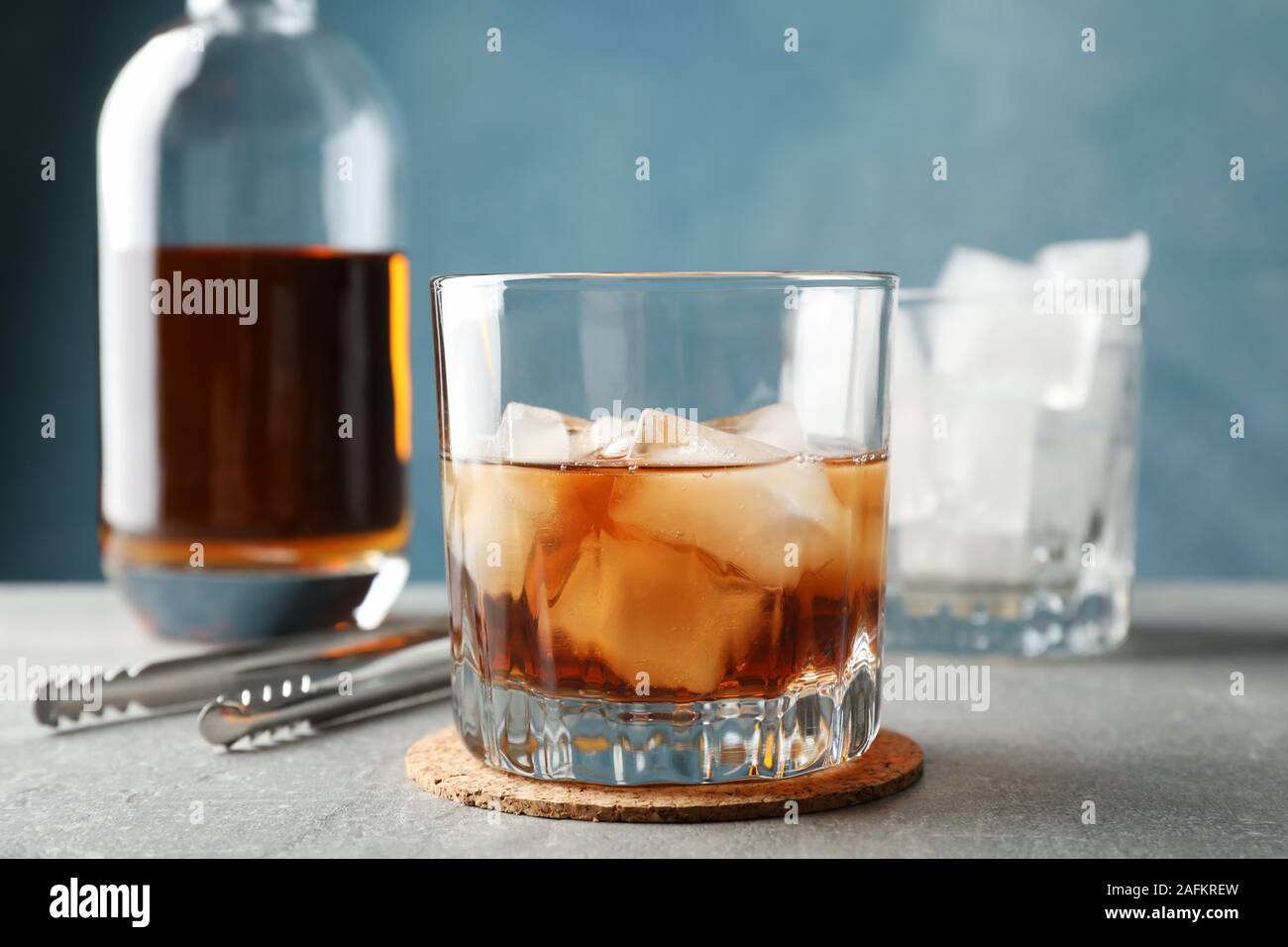 Bottle, glasses with ice cubes and whiskey on grey background, space for text Stock Photo