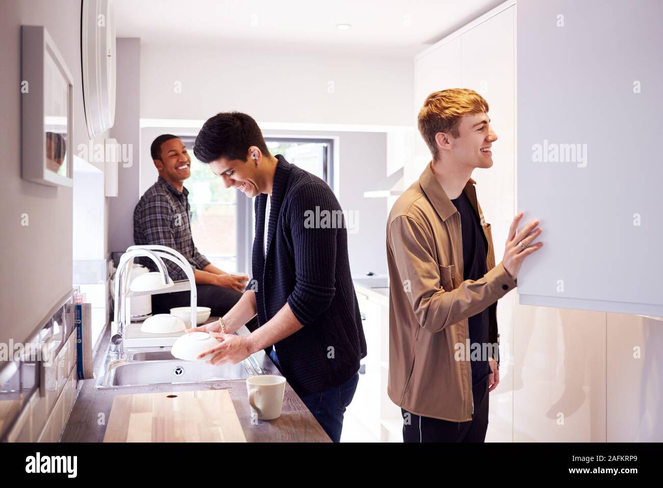 Group Of Male College Students In Shared House Kitchen Washing Up And Hanging Out Together Stock Photo