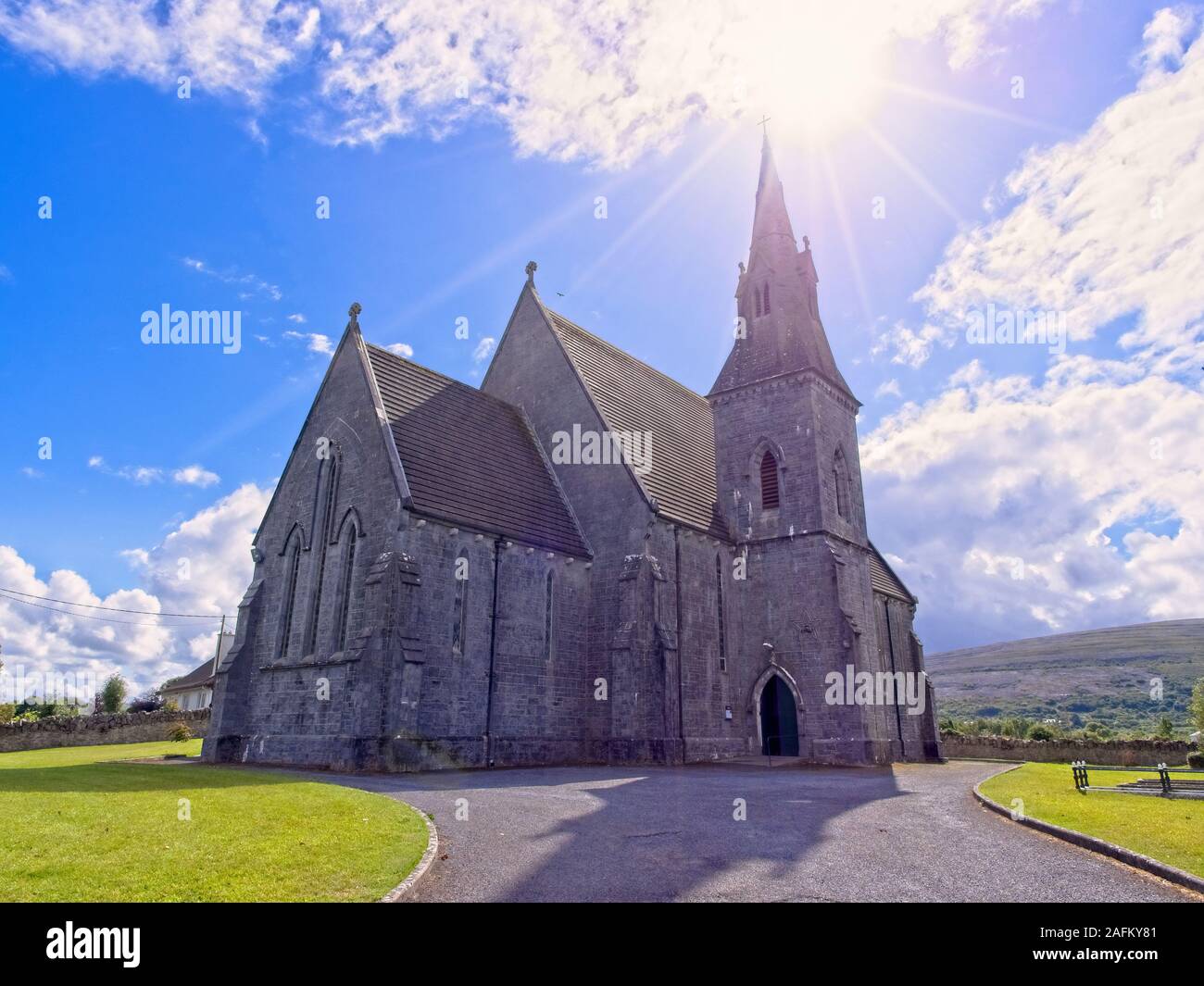 Saint John The Baptist Catholic church with a beautiful sky and a sunstar near Ballyvaughan, County Clare, Republic of Ireland Stock Photo