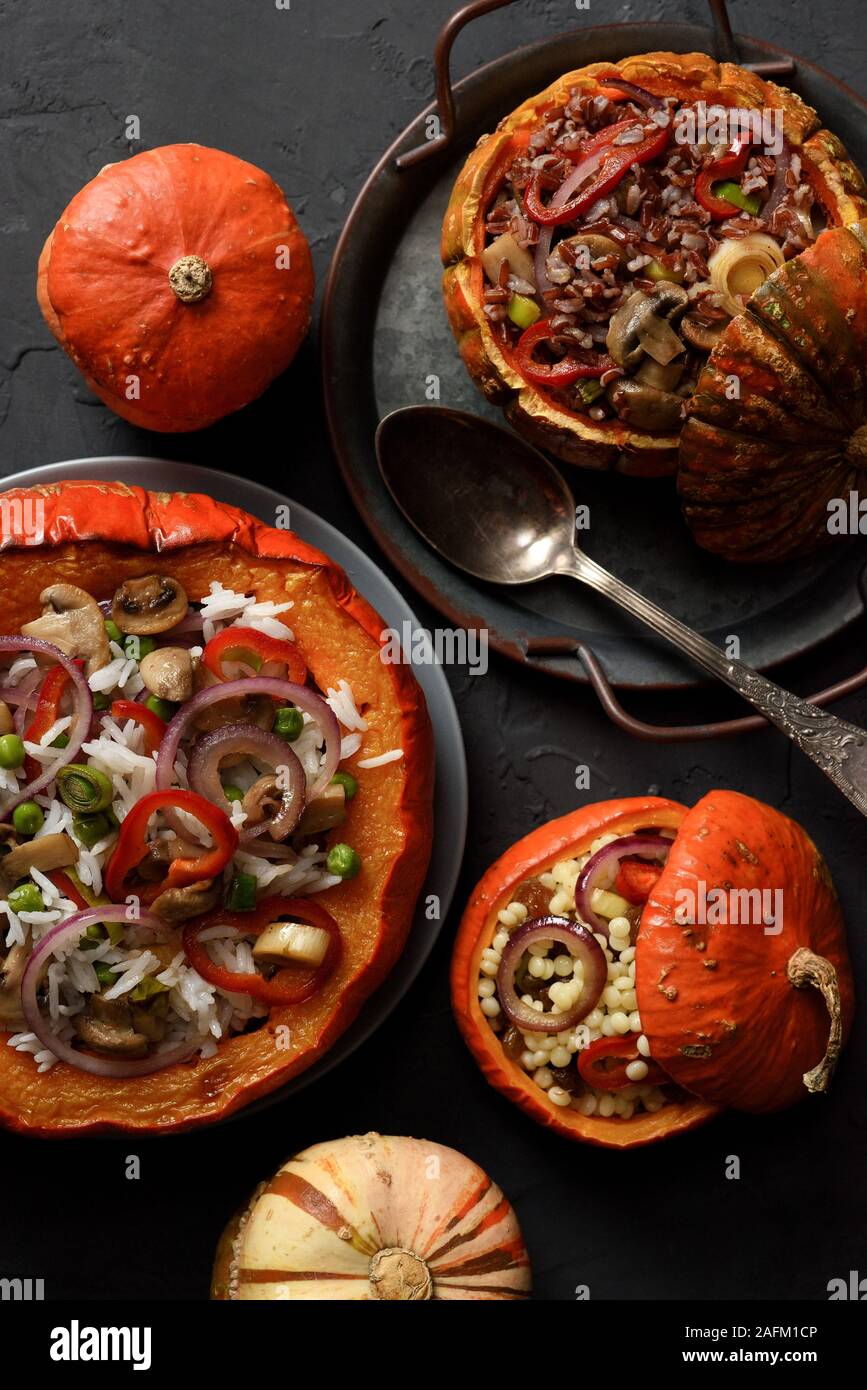 Healthy vegetarian food. Big and small pumpkins baked with brown and white rice, pearl couscous, peas, mushrooms, pepper and onion on black background Stock Photo