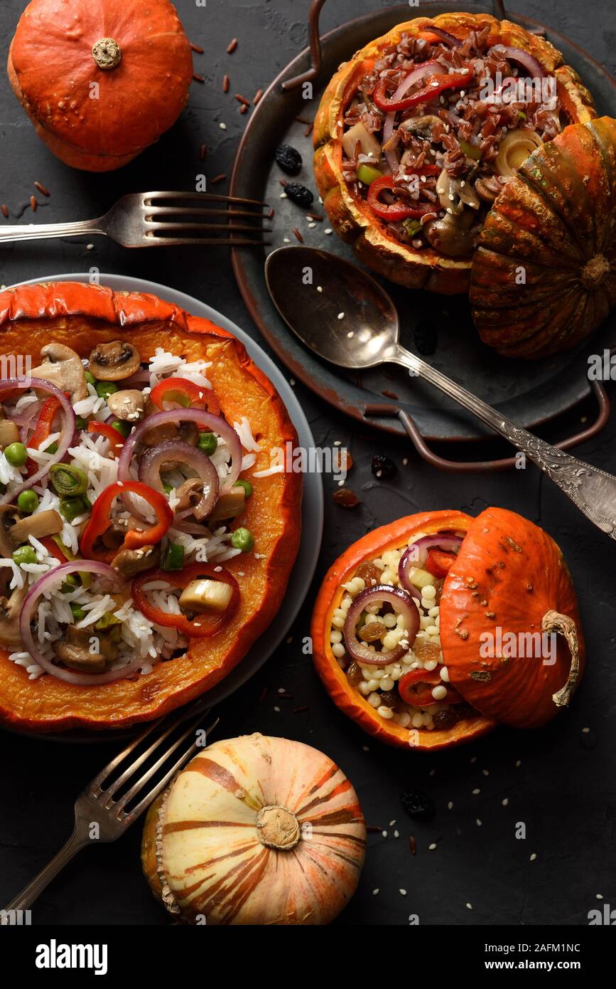 Healthy meat free food. Big and small pumpkins stuffed with brown and white rice, pearl couscous, peas, mushrooms, pepper and onion on black backgroun Stock Photo
