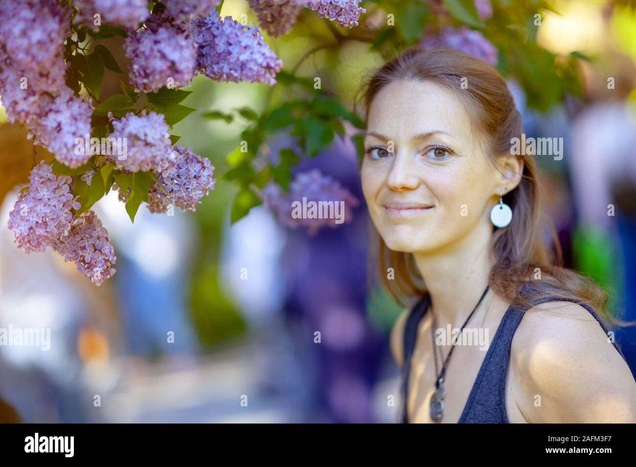 Young beautiful woman enjoying the smell of blooming lilac on a sunny day. Outdoor portrait in a blooming spring park Stock Photo