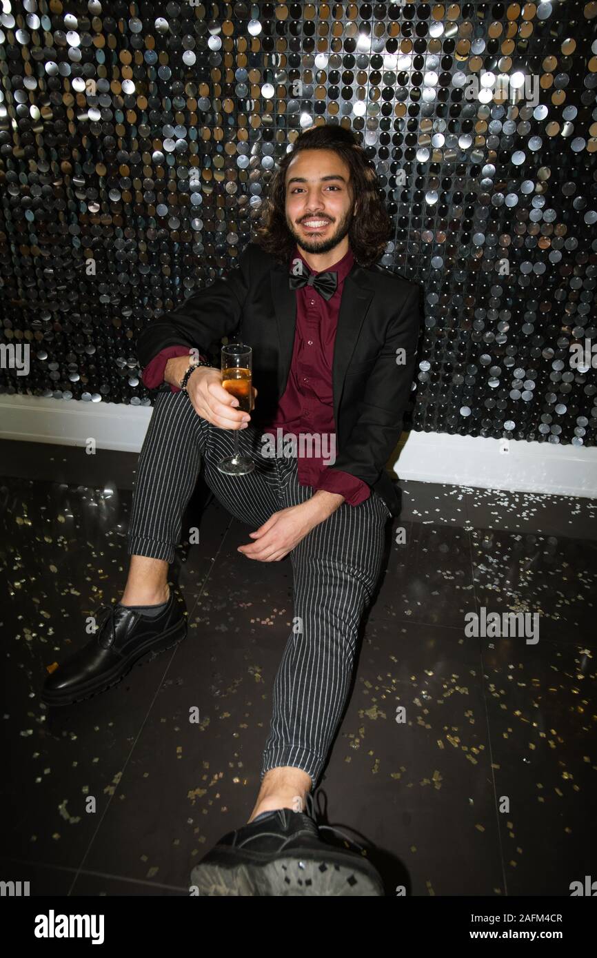 Young elegant man in suit toasting with champagne while sitting on the floor Stock Photo