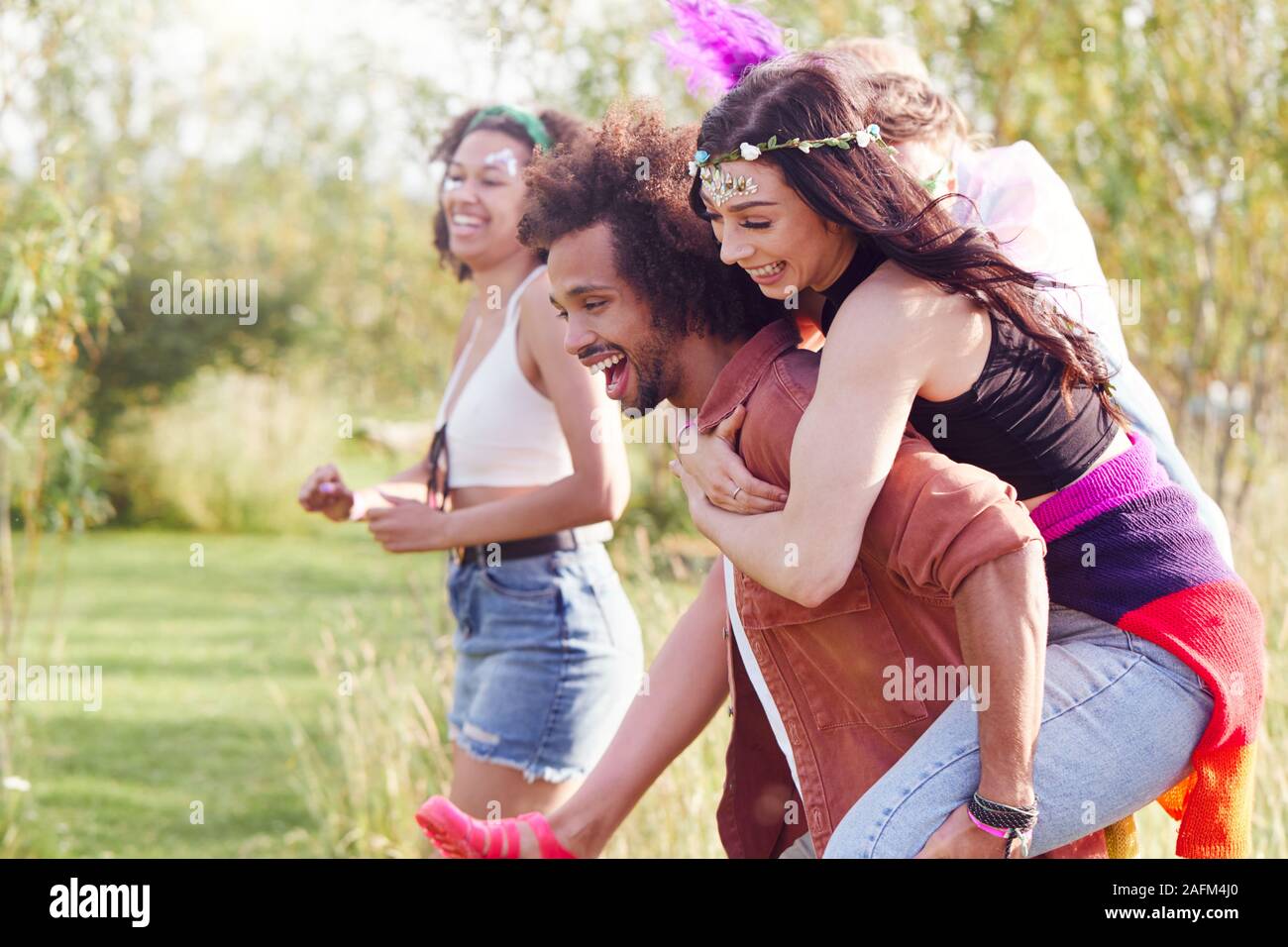 Group Of Friends Walking Back To Tent After Outdoor Music Festival With Men Giving Women Piggybacks Stock Photo