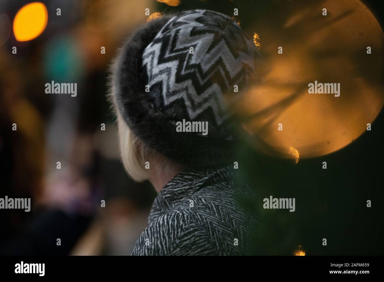 close up of a lady's head looking away, dressed in a winter hat and a coat with Christmas lights the background and foreground. Stock Photo
