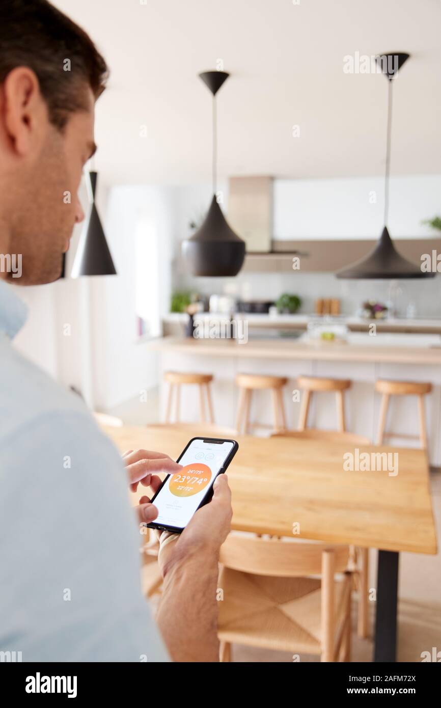 Man Using App On Smart Phone To Control Central Heating Temperature In House Stock Photo