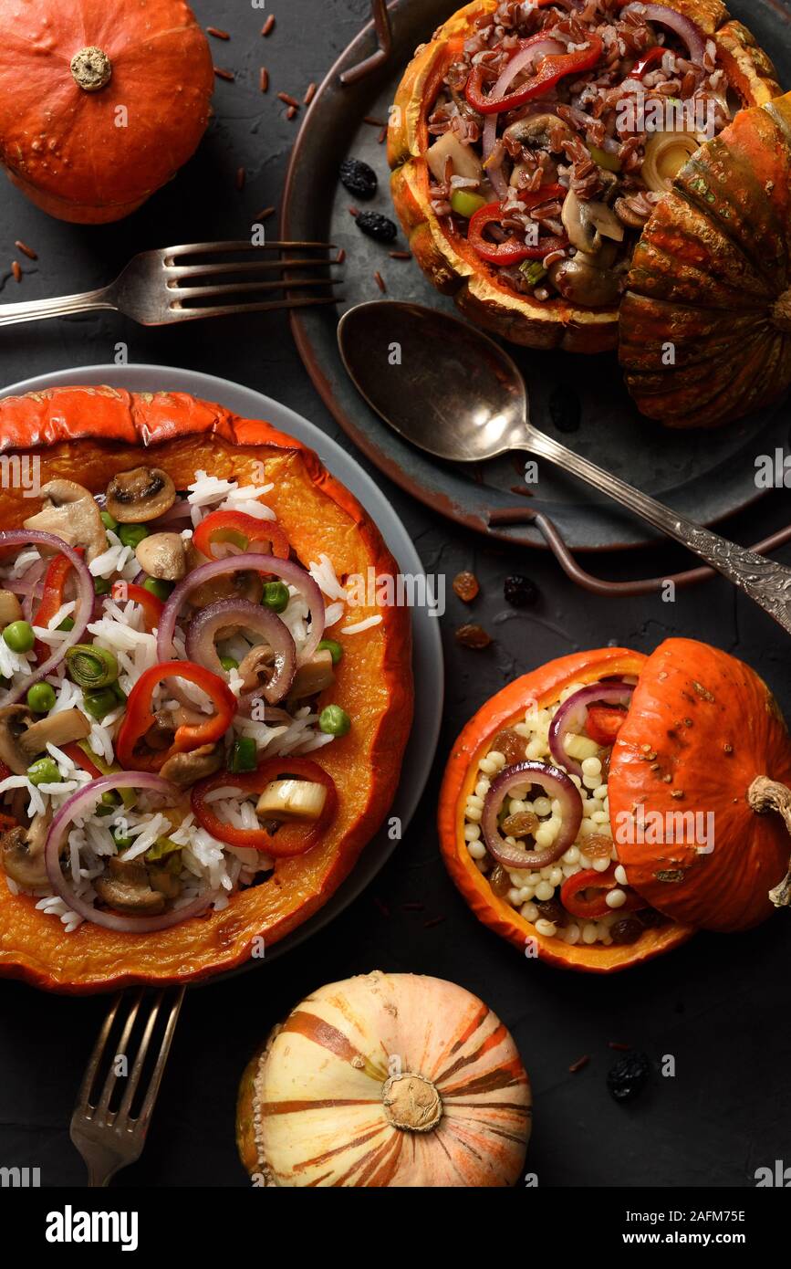 Healthy meat free meal. Pumpkins stuffed with rice, mushrooms, peppers and pearl couscous with vintage tray and cutlery on black background top view Stock Photo