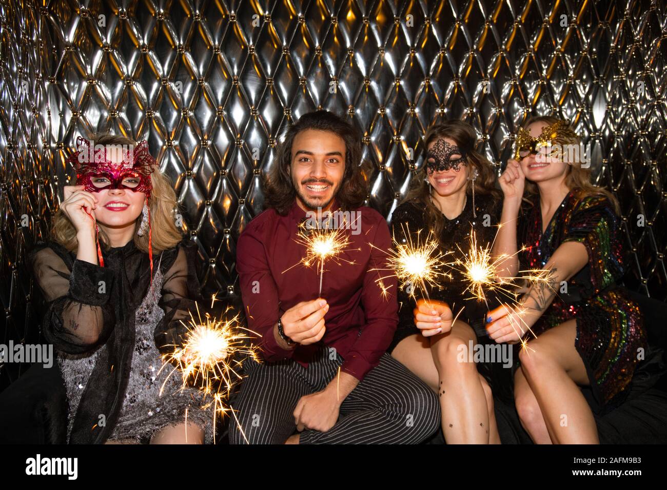 Three happy girls in venetian masks and guy holding sparkling bengal lights Stock Photo